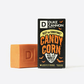 Duke Cannon Candy Corn Big Ass Brick soap in vibrant orange displayed next to black Halloween-themed packaging with dripping orange "Candy Corn" text and decorative bat graphics