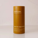 Routine Bonita Applebom deodorant in a mustard-yellow cylindrical paper tube with white “bonita applebom” branding, standing on a beige surface against a matching beige backdrop.