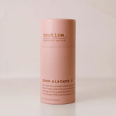 Routine Moon Sisters deodorant stick in blush‑pink paper tube with brown “moon sisters” branding, standing on a beige surface against a matching beige backdrop.