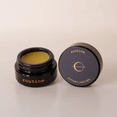 Routine The Class botanic perfume balm - open black glass jar showing golden-yellow solid perfume with navy blue lid featuring circle logo