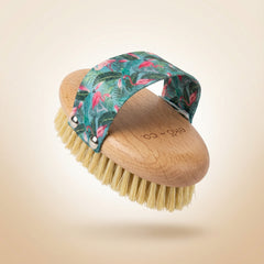 dry body brush shown at angle displaying natural sisal bristles and beechwood handle with flamingo strap arched over top