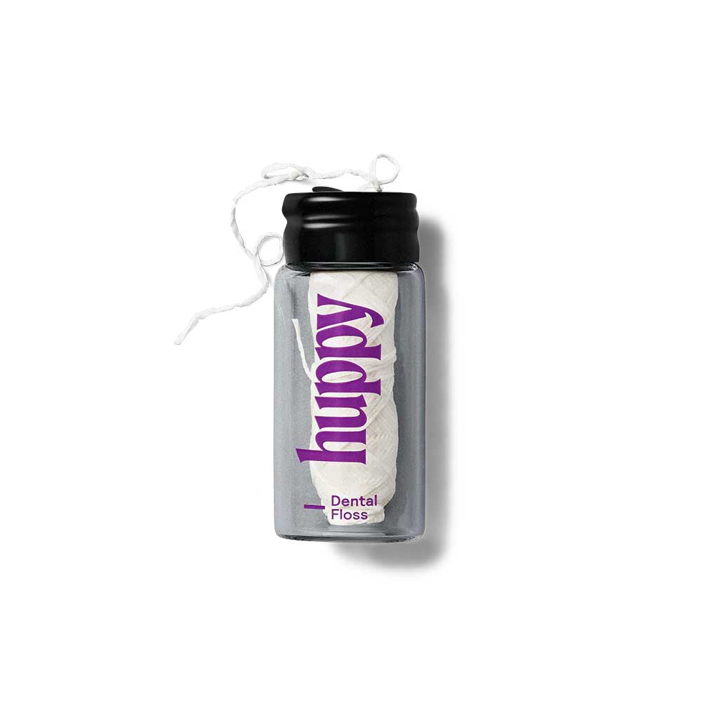 huppy dental floss - clear glass jar with black lid containing white floss spool, displaying purple huppy branding on minimalist white background