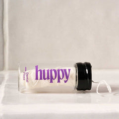 huppy dental floss jar lying on its side on white surface, showcasing the sleek glass container design and purple branding with floss visible inside