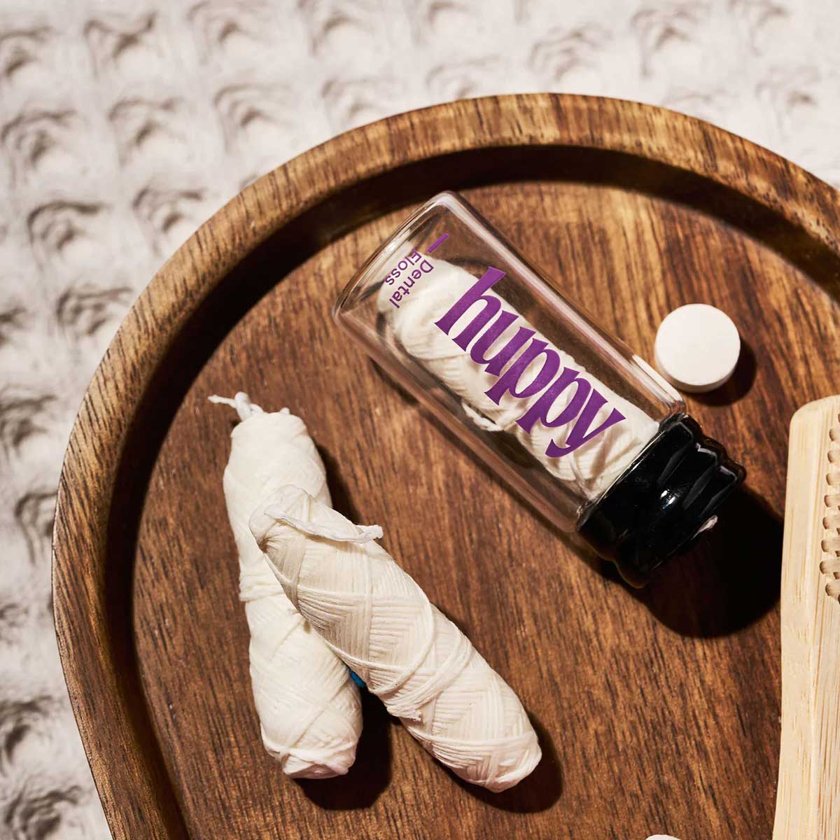 huppy dental floss flat lay styling - glass jar positioned on wooden tray with natural elements, highlighting sustainable packaging and elegant bathroom aesthetic
