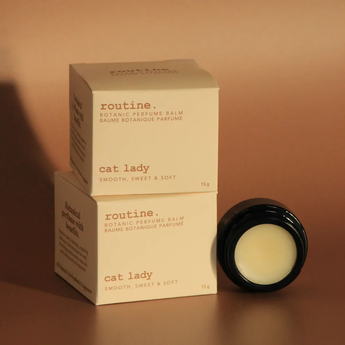 Routine Cat Lady perfume collection - multiple cream-coloured product boxes stacked with black glass jar showing coconut pineapple vanilla scented balm - botanic perfume gift set