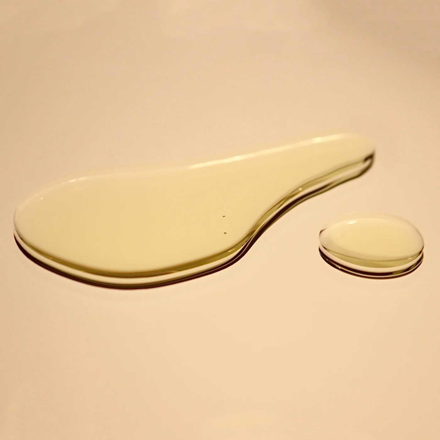 Close-up of golden-amber routine body oil texture showing smooth, clear botanical oil consistency with single drop demonstrating lightweight viscosity.