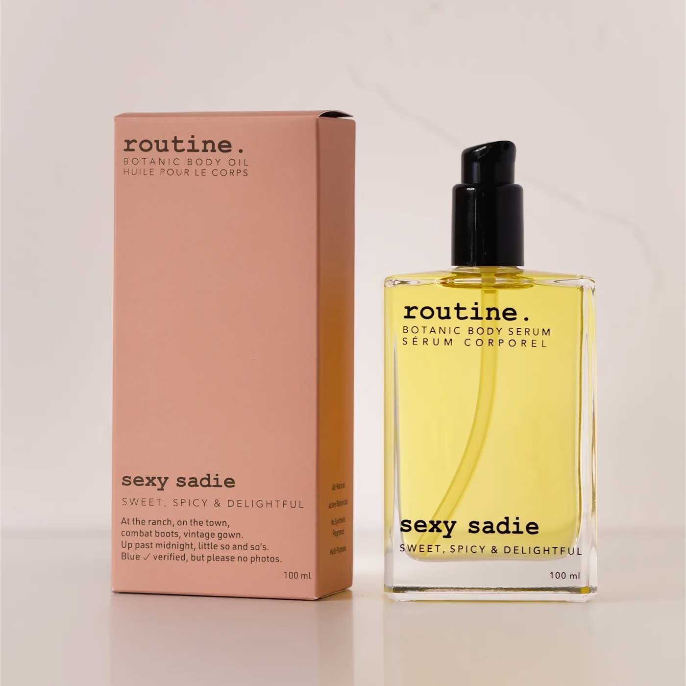 routine Sexy Sadie Botanic Body Oil in 100ml glass bottle with black pump next to dusty rose cardboard packaging showing sweet, spicy & delightful scent description
