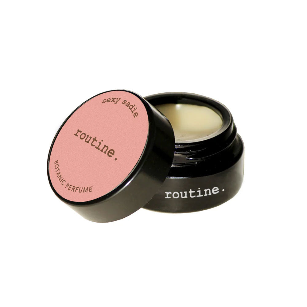 Routine Sexy Sadie solid perfume - black glass jar with coral-pink label open revealing golden balm texture - natural ylang ylang sweet orange vanilla cinnamon scented moisturizing perfume
