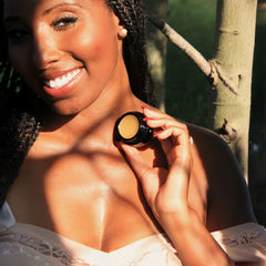Woman holding Routine Sexy Sadie solid perfume - smiling model holding open black jar showing golden balm in natural sunlight