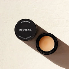 Routine Superstar solid perfume - black glass jar with lid next to jar showing golden balm in natural lighting - warm rich iconic botanical fragrance balm