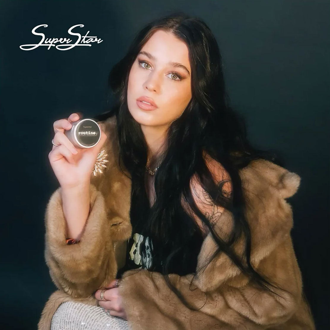 Fashion model holding Routine Superstar solid perfume - woman in luxurious fur coat displaying black glass jar with SuperStar branding - iconic signature fragrance lifestyle image