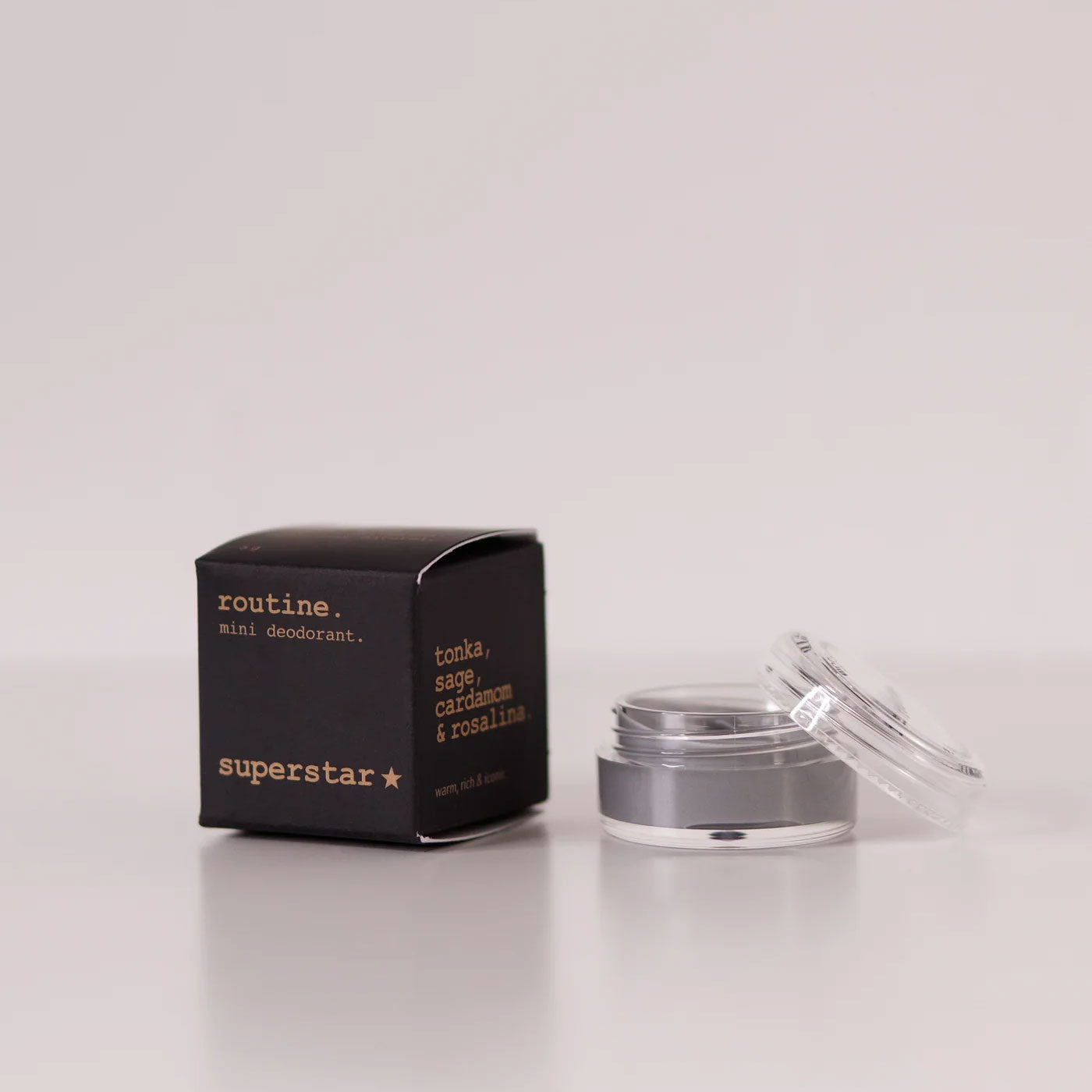 Routine Superstar mini deodorant showing black packaging with gold text next to open glass jar containing charcoal-grey natural deodorant with activated charcoal