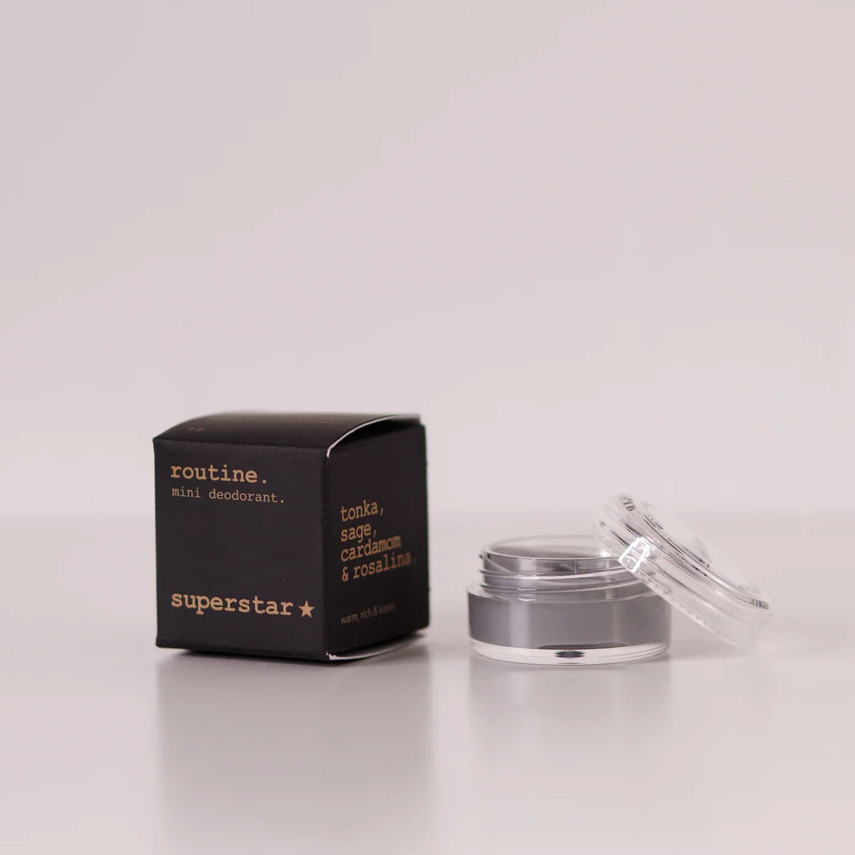 Routine Superstar mini deodorant showing black packaging with gold text next to open glass jar containing charcoal-grey natural deodorant with activated charcoal