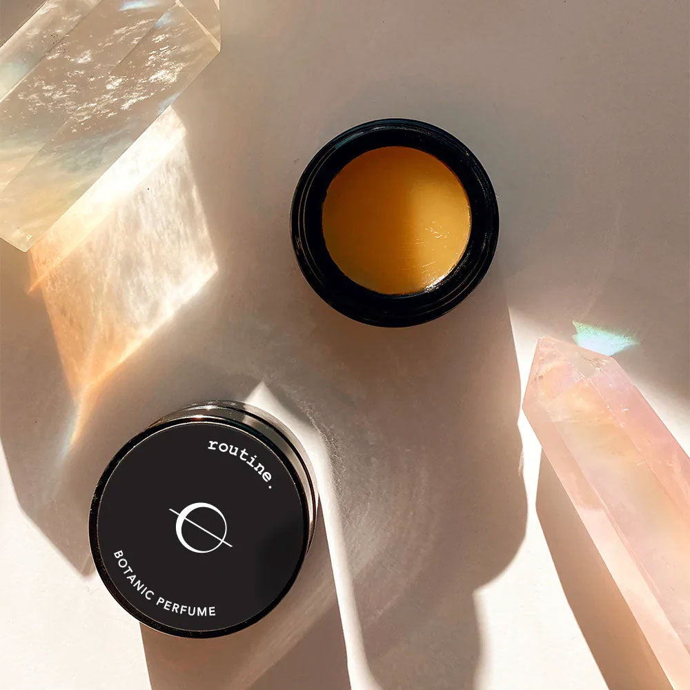 Routine The Class solid perfume - overhead view of black jar with navy lid beside crystals in natural lighting