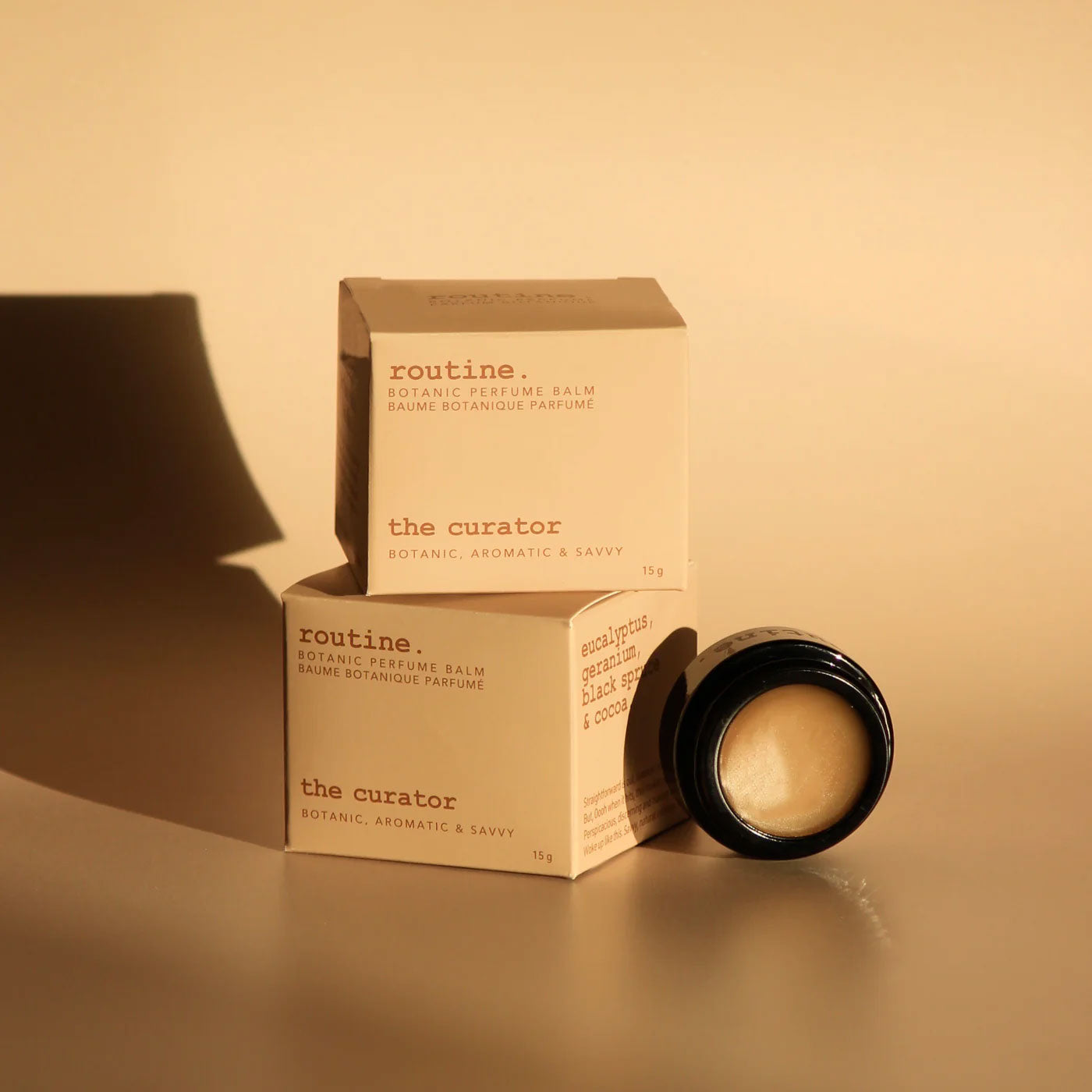 Routine The Curator perfume collection - multiple cream-coloured product boxes with botanical scent details and black glass jar in warm lighting - sophisticated aromatic solid perfume balm