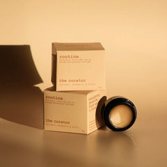 Routine The Curator perfume collection - multiple cream-coloured product boxes with botanical scent details and black glass jar in warm lighting - sophisticated aromatic solid perfume balm